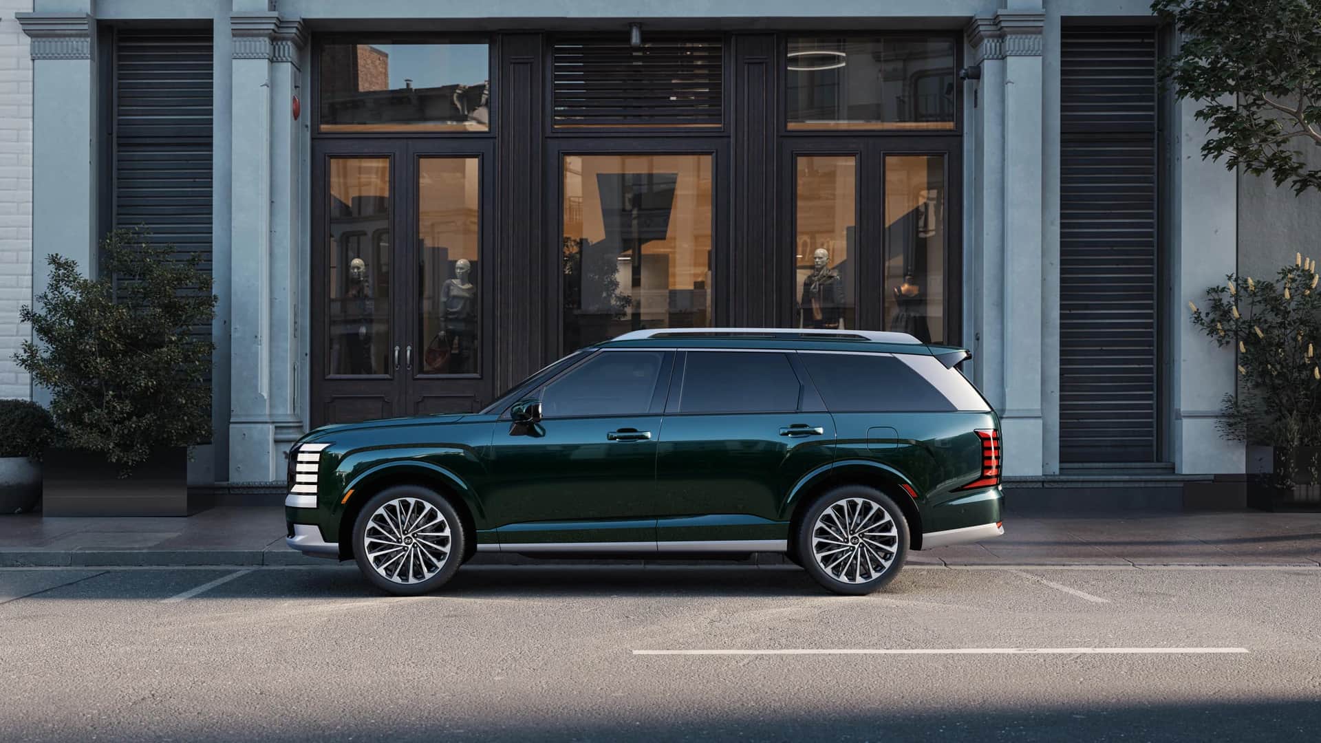 Dark green 2026 Hyundai Palisade in profile, parked on a downtown street in front of a stone facade
