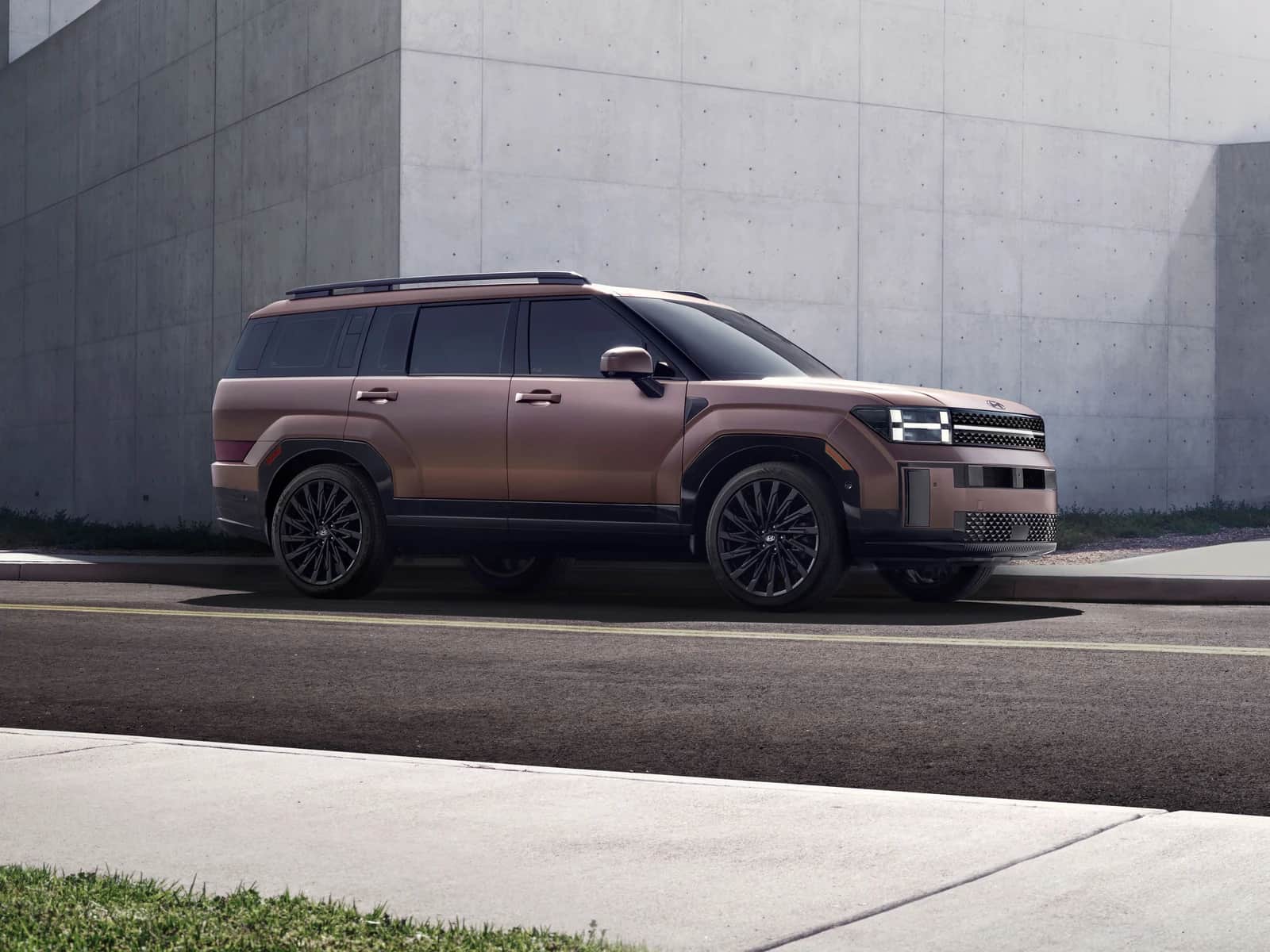 Copper 2026 Hyundai Santa Fe, front three-quarter view, parked along a large contemporary concrete wall under a clear sky