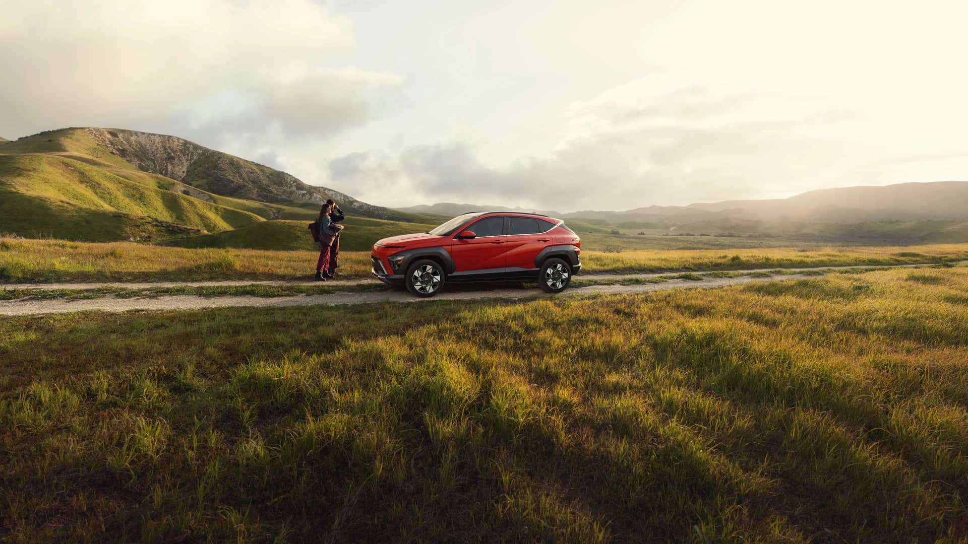 Hyundai KONA 2026 orange sur un chemin de campagne dans un grand champ, collines au soleil couchant