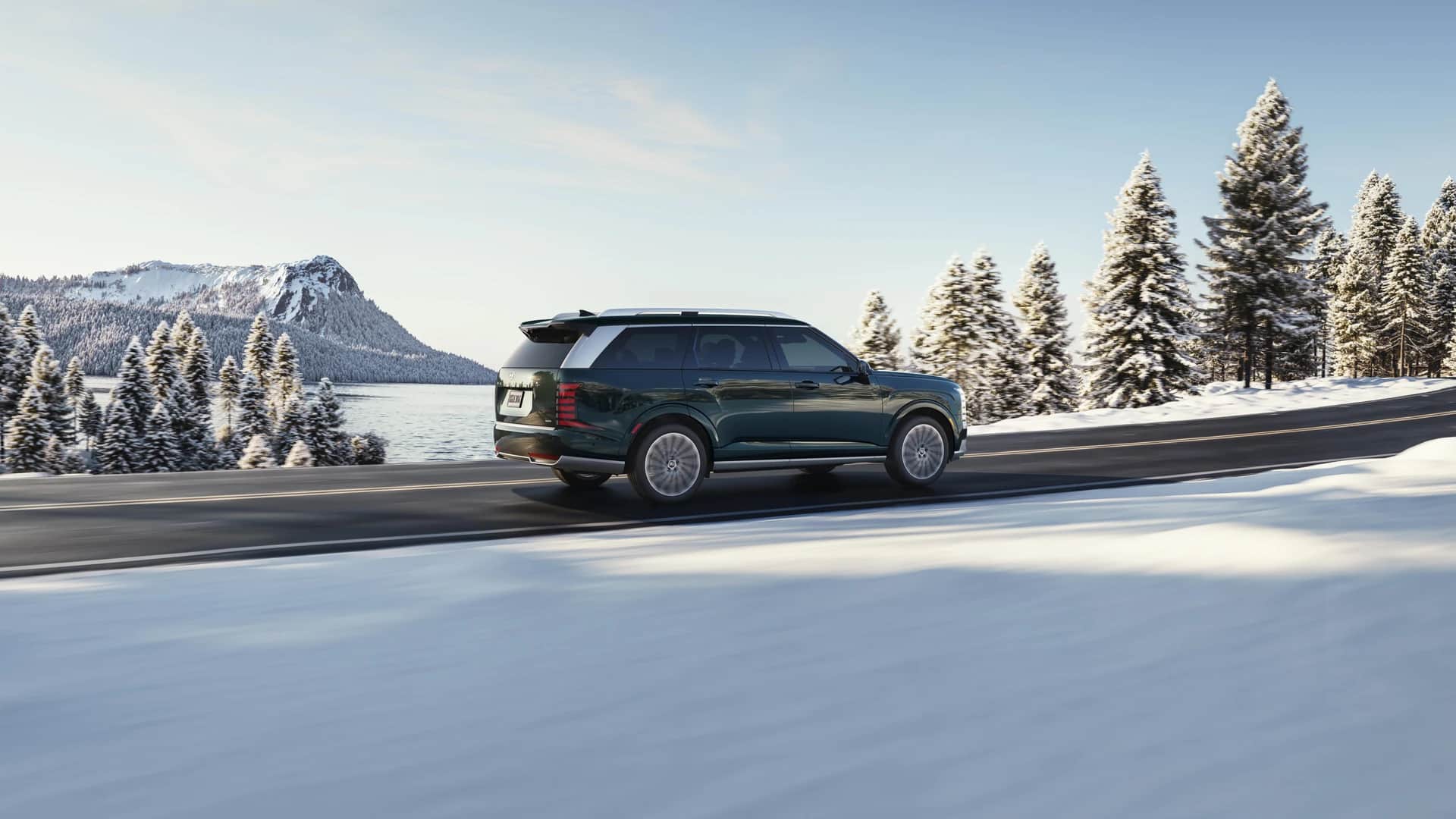 Hyundai Palisade 2026 sur une route enneigée, sapins blancs, lac et montagne en arrière-plan