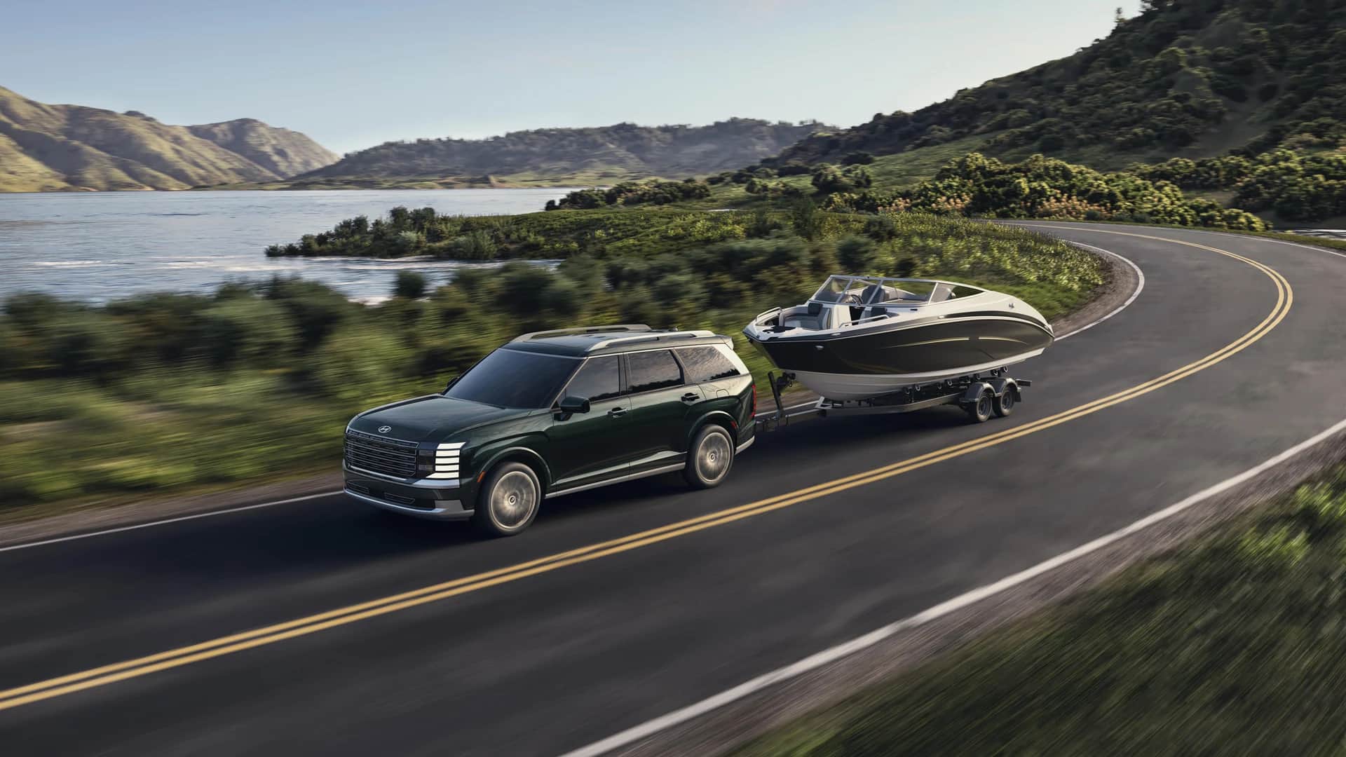 Hyundai Palisade 2026 qui tire un bateau sur une route qui longe un lac, collines boisées